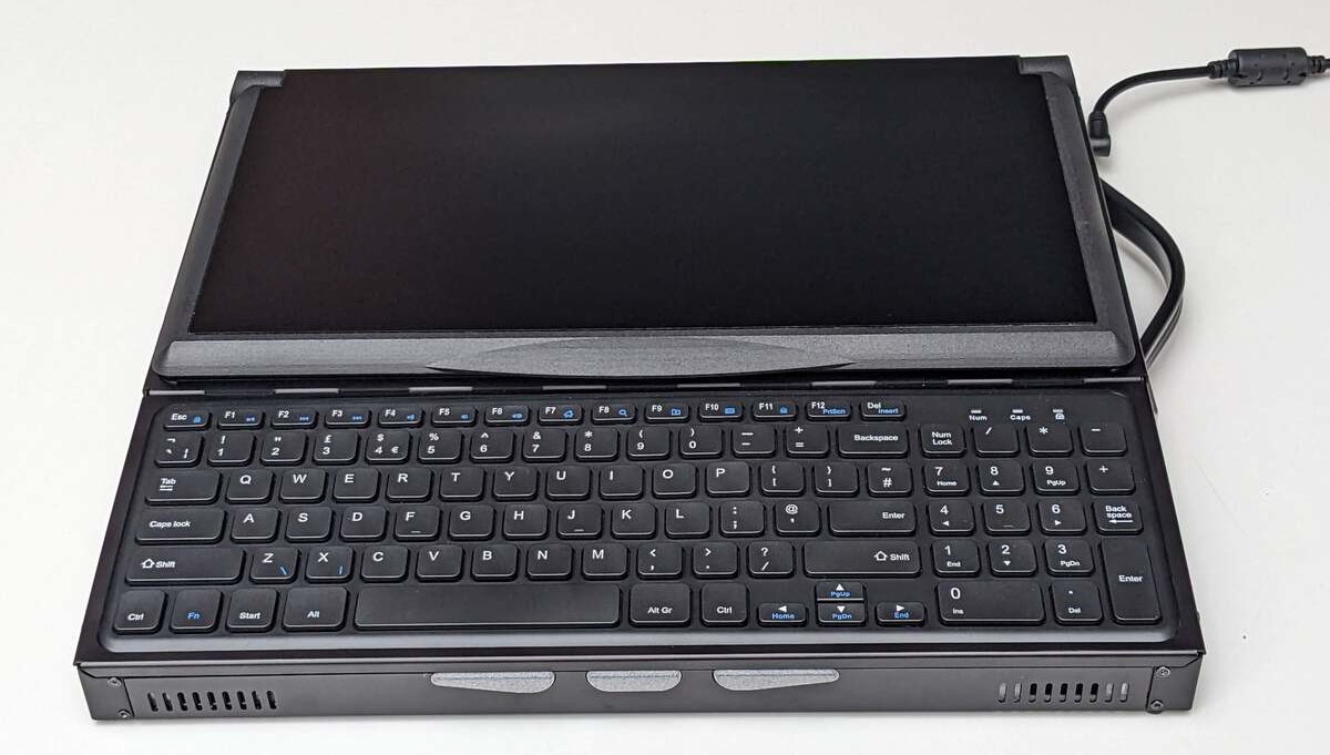 Front on photo of the Canute Scientific when closed. Three light grey thumb buttons situated in front of the full sized keyboard, with speaker grills to either side and screws for replacing or modifying the whole front panel.